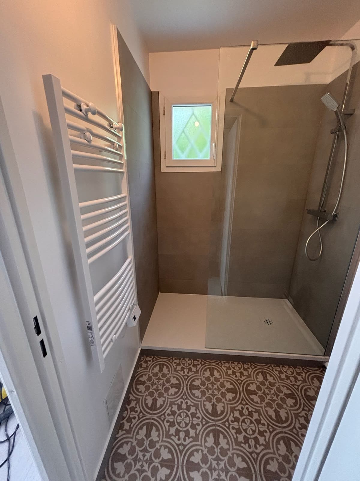 Douche, petite fenêtre et sol à motifs de la salle d’eau terminée