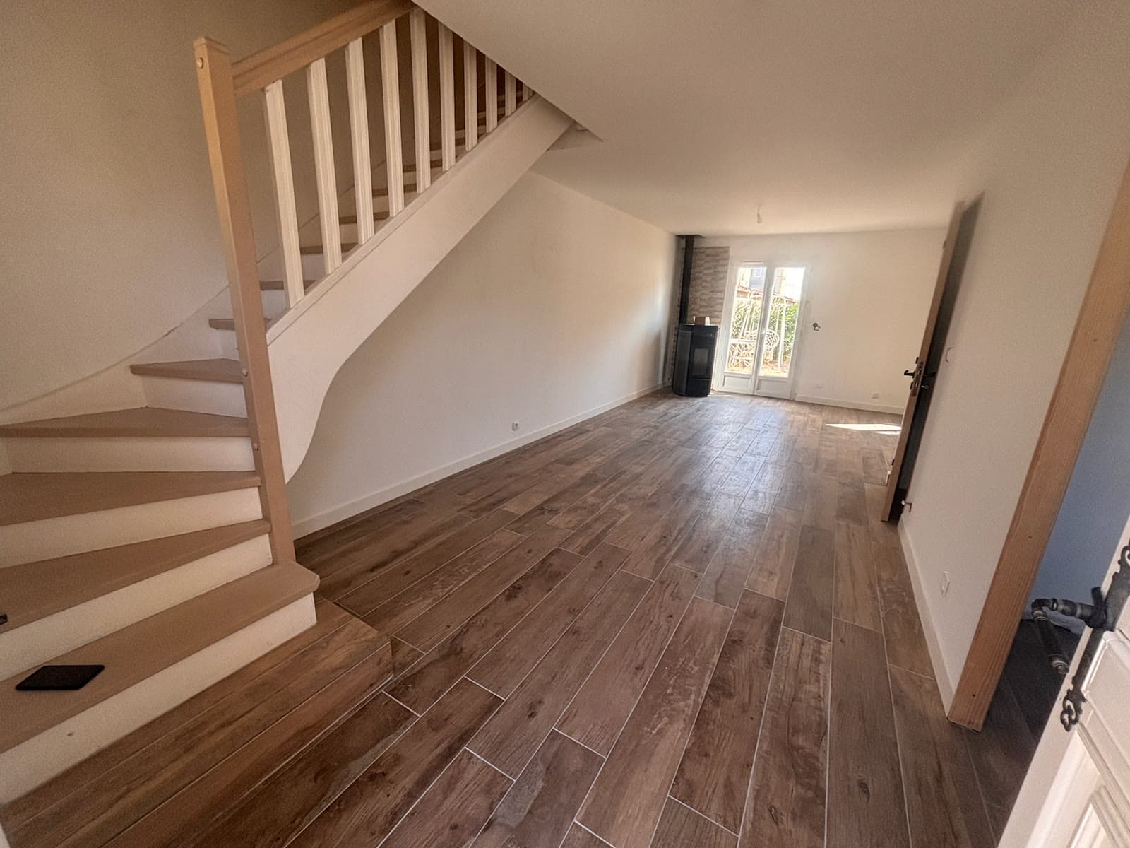 Vue de la même pièce rénovée depuis l’entrée, avec escalier et poêle
